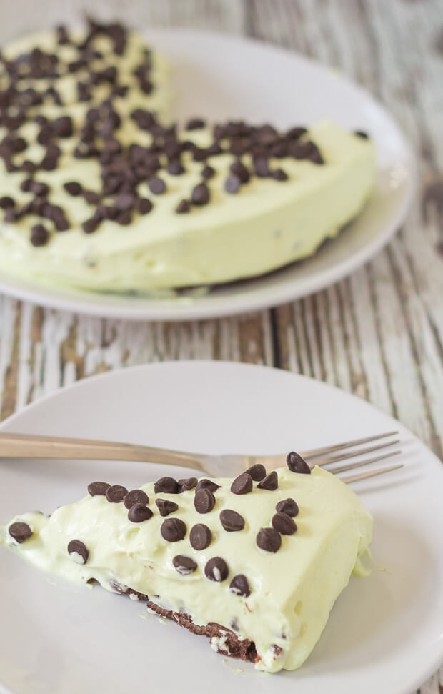 A slice of no bake mint chocolate chip cheesecake on a plate with a fork. Rest of the cheesecake in the background.