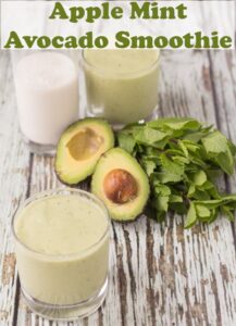 A glass of apple mint avocado smoothie with a halved avocado, bunch of mint and another glass of the smoothie and a glass of milk in the background. Pin title text overlay at top.