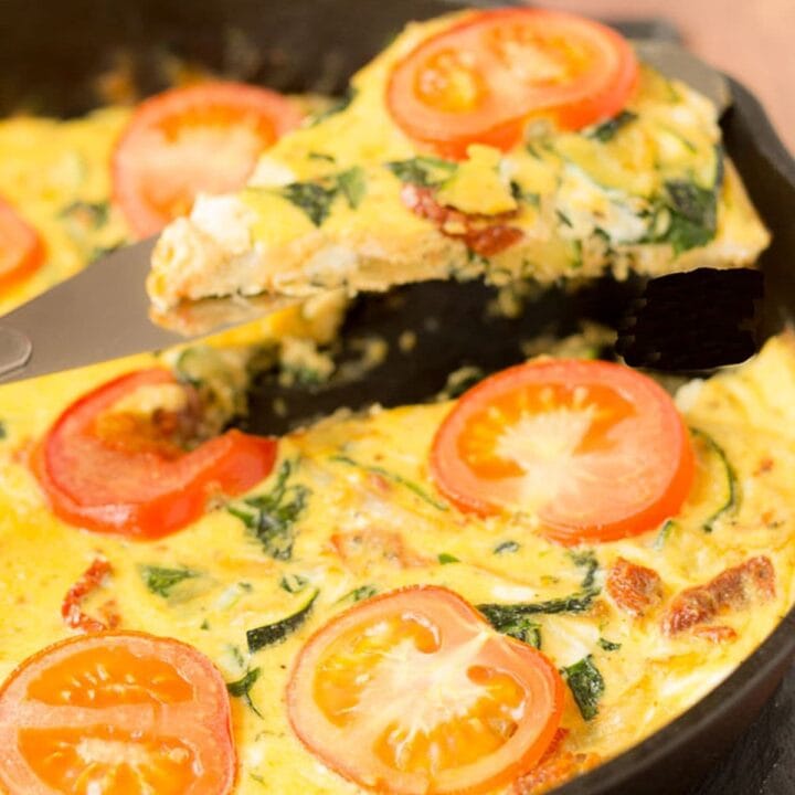 A slice of courgette and sundried tomato frittata being lifted from the skillet it was cooked in.
