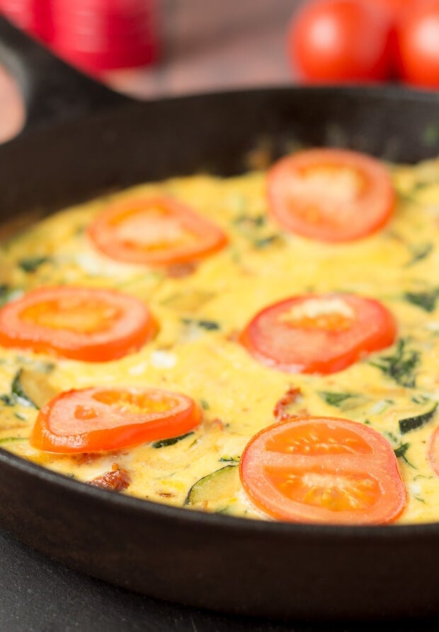 Close up of a skillet of cooked courgette and sundried tomato frittata.