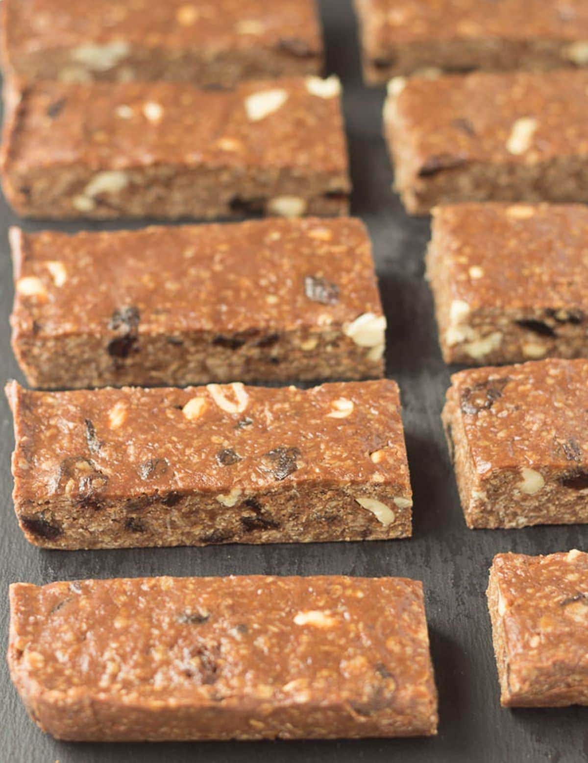 Two lines of no bake chocolate peanut butter raisin oat bars on a black slate.