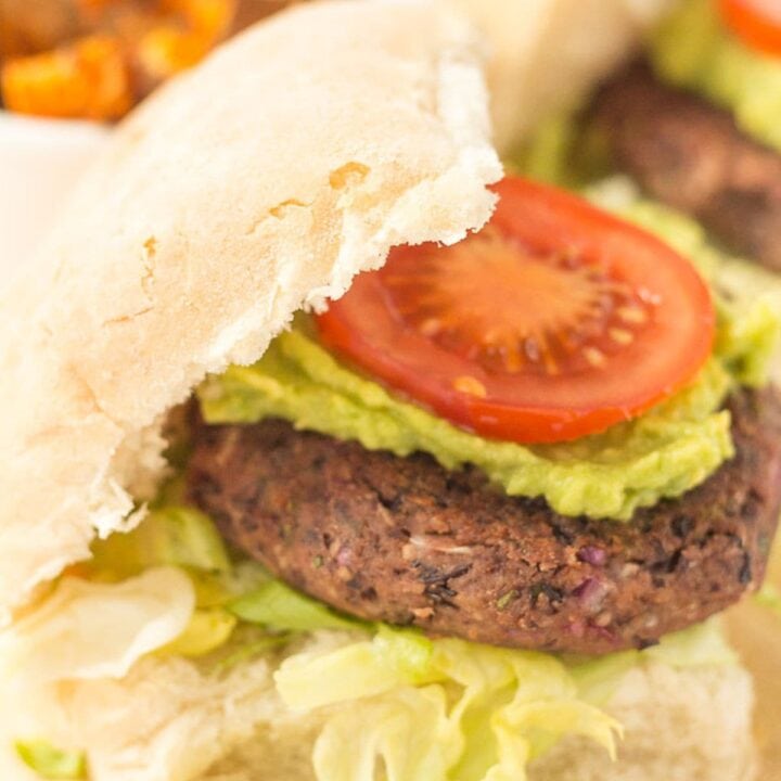 A quick and easy black bean burger in a burger bun topped with avocada and a sliced tomato.