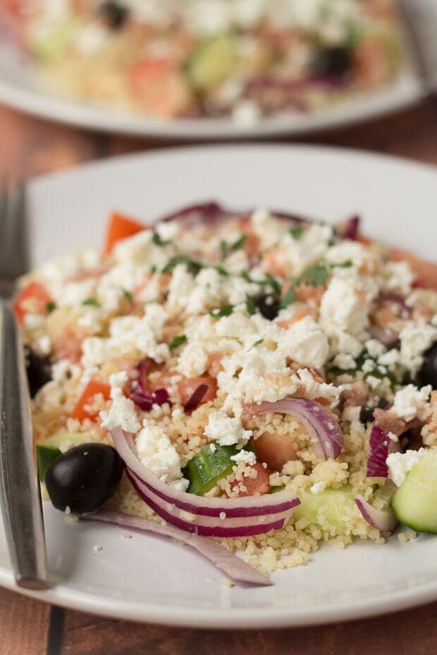 Close up of a plate with couscous Greek salad served on it and a fork to the side.