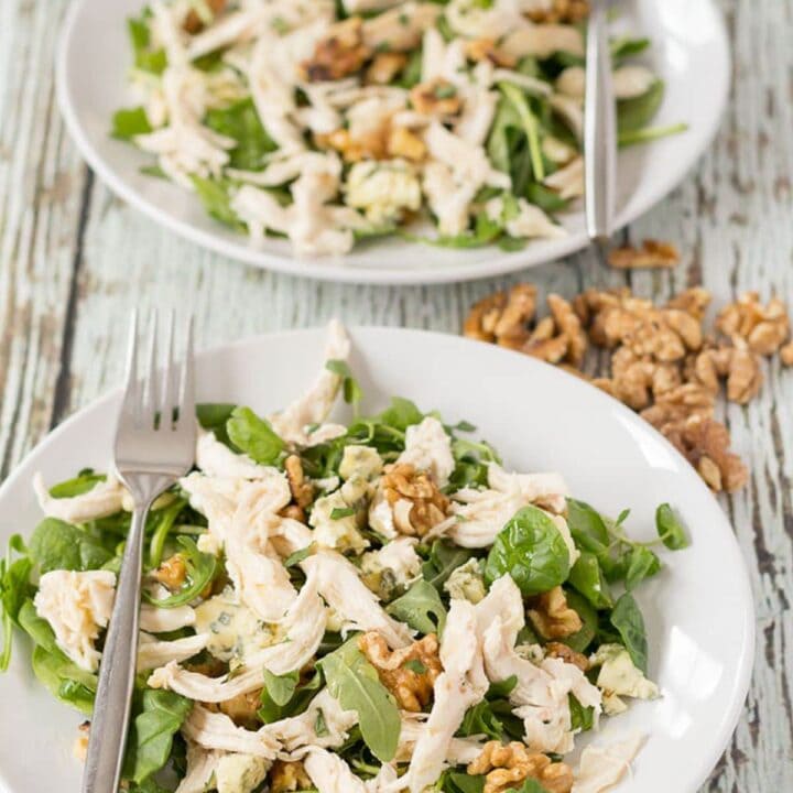 Two plates of chicken walnut and blue cheese salad one in front of the other with forks on and walnuts for decoration in between.