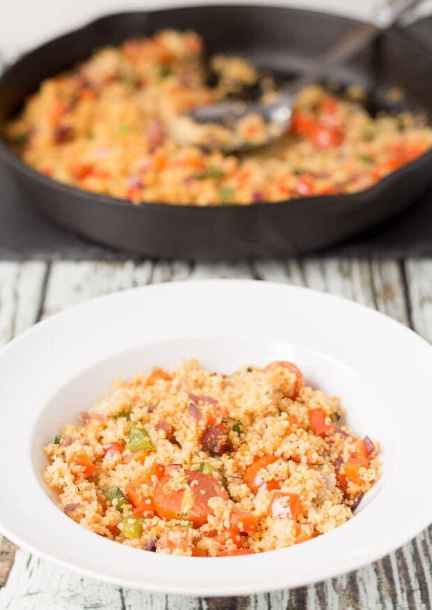 A plate of Mediterranean chorizo couscous. Rest of the cooked dish in a large pan in the background with a serving spoon in.