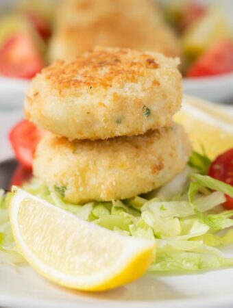 Two quick healthy fish cakes stacked on a bed of iceberg lettuce with a lemon wedge in front.