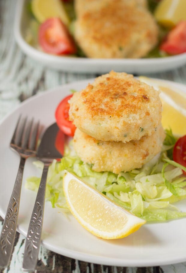 A plate with two quick healthy fish cakes stacked on a bed of iceberg lettuce. Fish knife and fork to the left side.