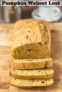Pumpkin and walnut loaf cake lying on a bread board, facing forward with 3 slices.