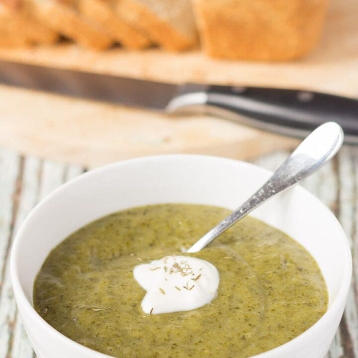 A bowl of curried potato and kale soup with a soup spoon in and dollop of yogurt on top. A sliced loaf of bread in the background.