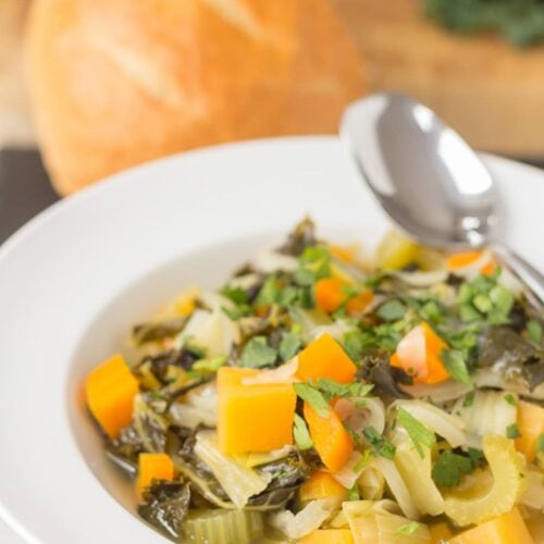 A bowl of Scottish vegetable stew with a spoon to the side. Part of a loaf of bread in the background.