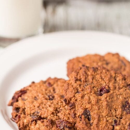 A plate of wholemeal chocolate cranberry cookies with a glass of milk behind.