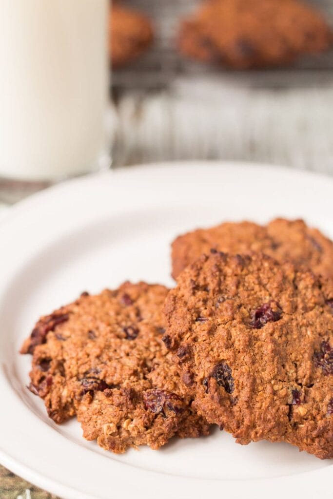 A plate of wholemeal chocolate cranberry cookies with a glass of milk behind.