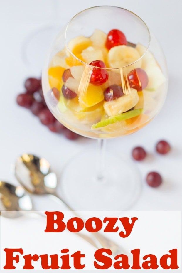 A glass of boozy fruit salad with a bunch of grapes behind. Pin title text overlay at bottom.