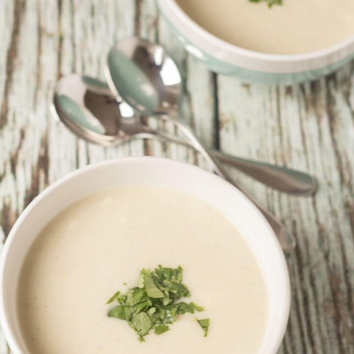 Birds eye view of two bowls of creamy cauliflower soup garnished with chopped coriander. Soup spoons in between.