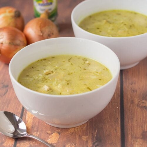 Two bowls of leftover turkey soup. A soup spoon in the foreground. A jar of herbs and three onions in the background.
