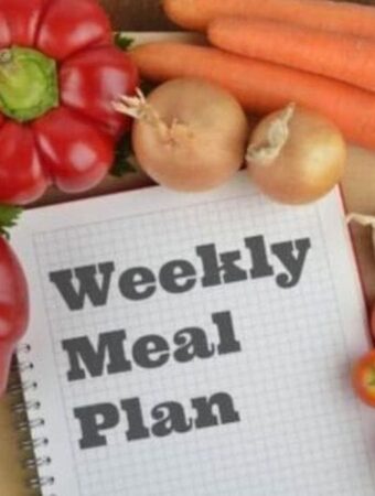 Weekly meal plan journal in centre of picture surrounded by vegetables.