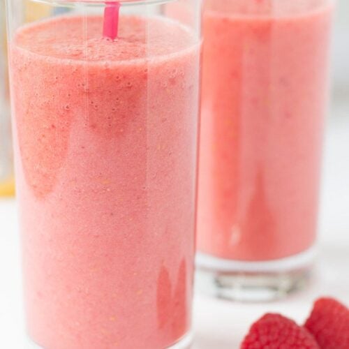 Two glasses of banana raspberry orange power smoothie with straws in. Three raspberries in front as decoration.