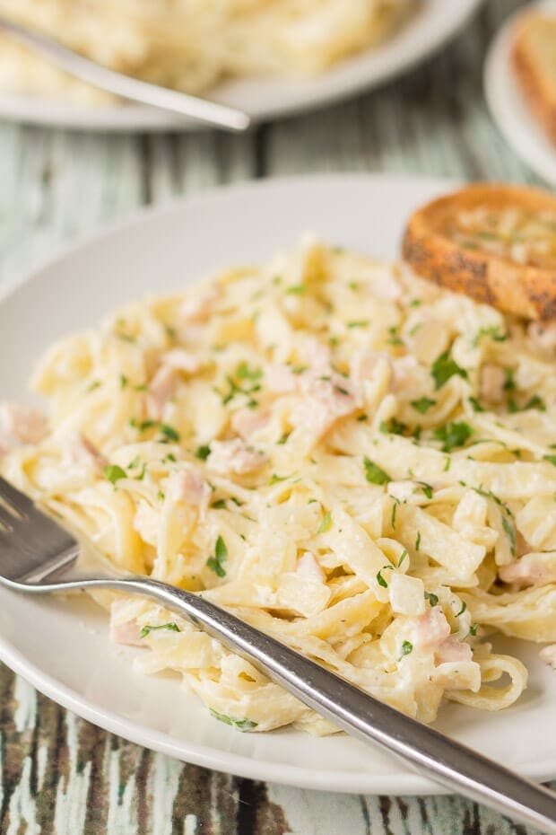 Close up of a plates of low fat tagliatelle carbonara with a fork to the side and a slice of garlic bread on.