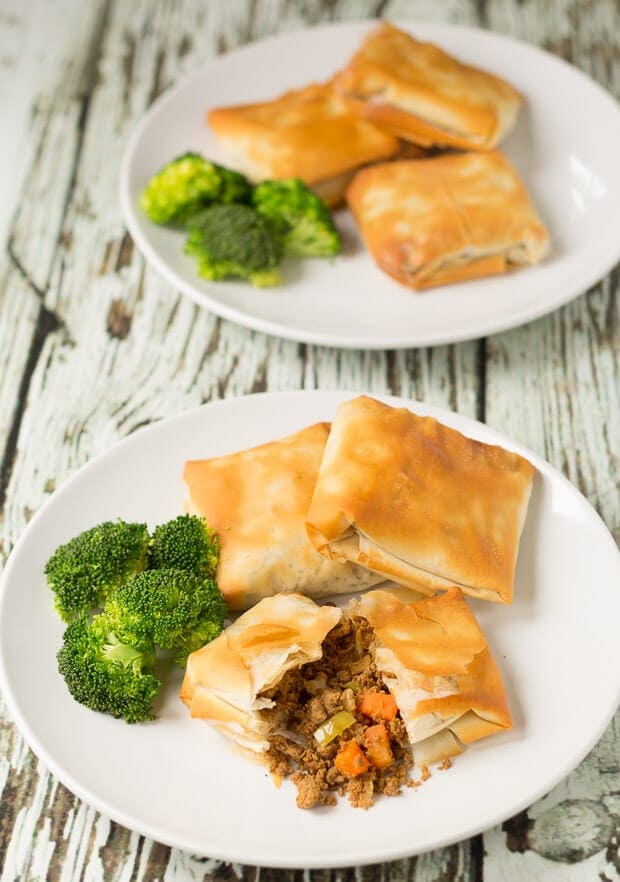Two plates one in front of the other with three spiced quorn filo pastry parcels on with broccoli. Front plate has one parcel cut in half to show filling.