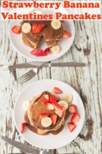 Two plates of strawberry banana valentines pancakes topped with chopped strawberries. Knife and forks to the front. Pin title text overlay at top.