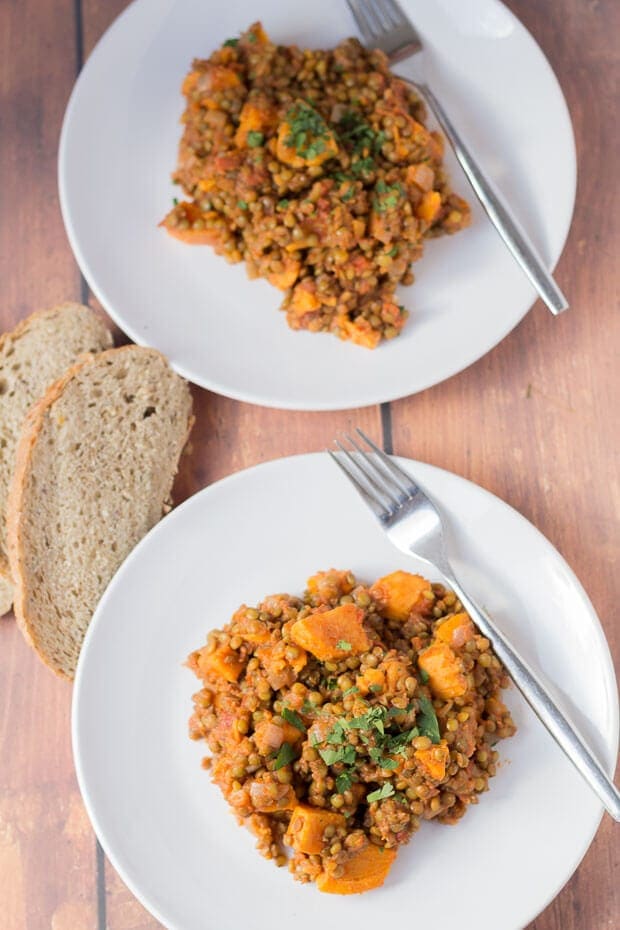 Birds eye view of two plates of green lentil and sweet potato stew with forks to the side and slices of bread in between.