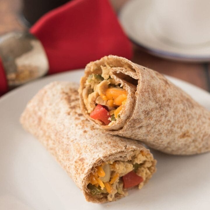 Two quick healthy breakfast burritos stacked on a plate. Cup, cafetiere and a red napkin in the background.