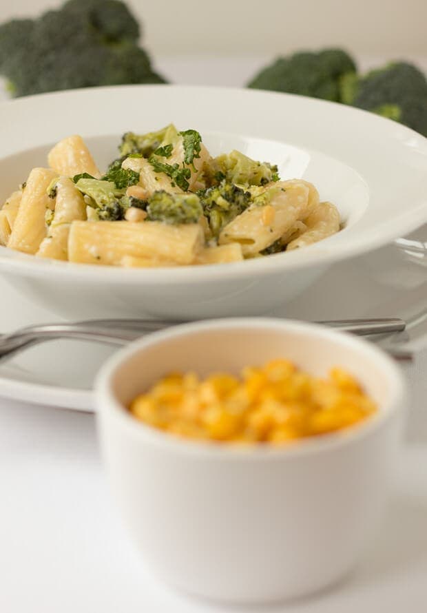 Rigatoni with broccoli and parmesan served in a white pasta bowl on a plate. A ramekin of sweetcorn at the front.