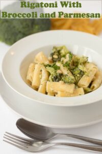 A bowl of rigatoni with broccoli and parmesan with a fork and spoon in front.