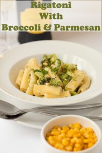 Rigatoni with broccoli and parmesan served in a white pasta bowl on a plate with a fork and spoon. Ramekin of sweetcorn to the front. Pin title text overlay at top.