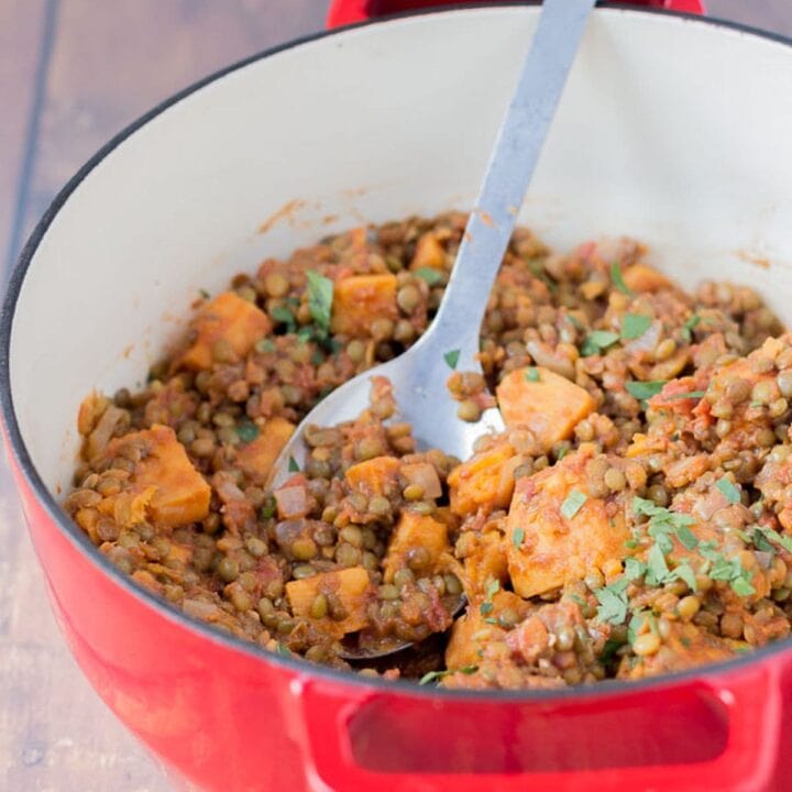 Green lentil and sweet potato stew in a casserole pot with a serving spoon.