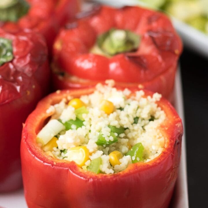 Close up of vegetarian couscous stuffed peppers sitting upright in a casserole dish showing the filling of the front pepper. Salad dish in the background.