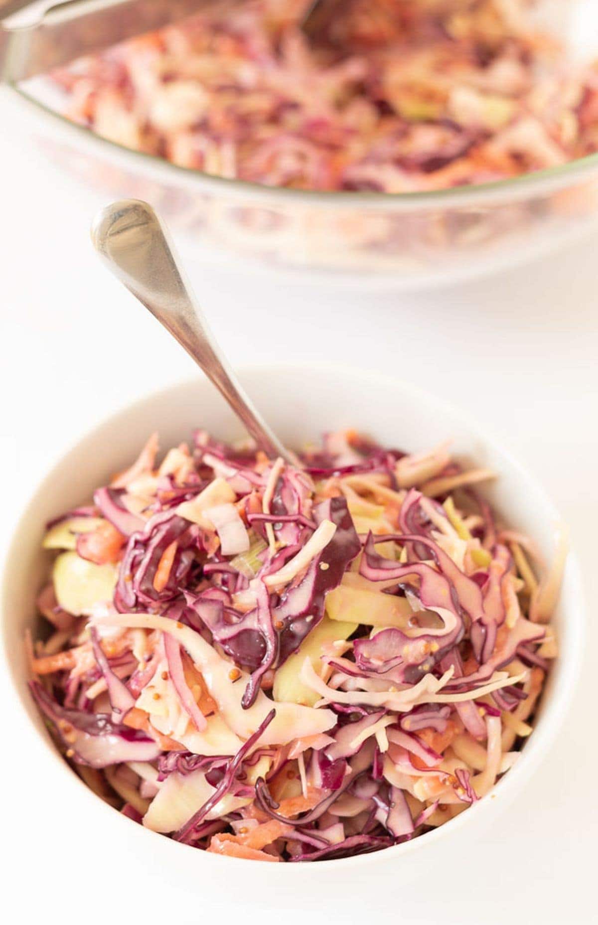 A bowl of easy healthier coleslaw with a serving spoon in.