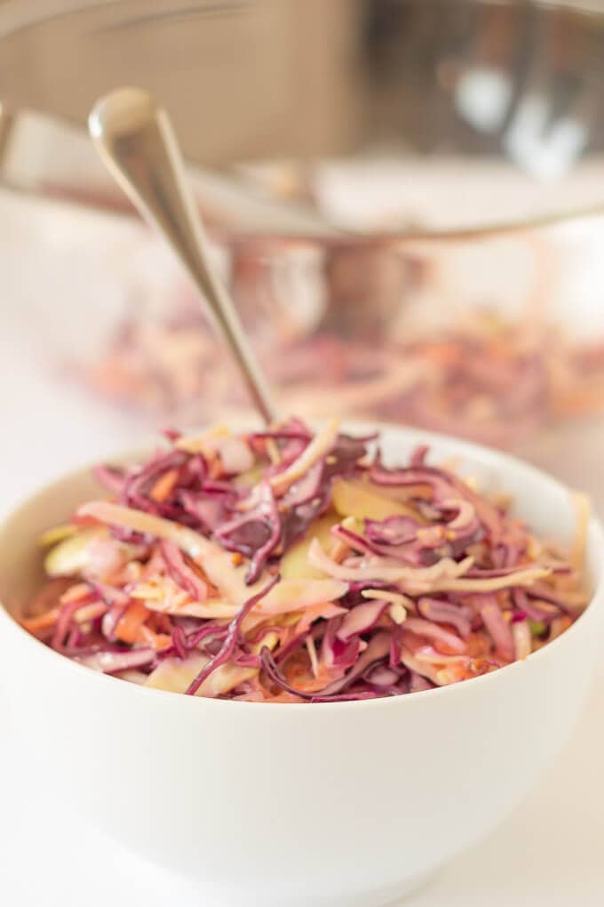 Close up of a bowl of easy healthier coleslaw with a serving spoon in.