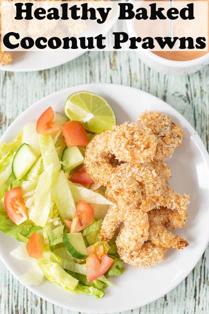 Healthy baked coconut prawns with dipping sauce on a white plate with a salad of iceberg lettuce, cucumber and tomatoes.