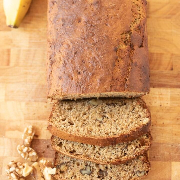 Birds eye view of healthy banana and walnut loaf on a chopping board. Three slices cut off and a banana and walnuts surrounding as decoration.