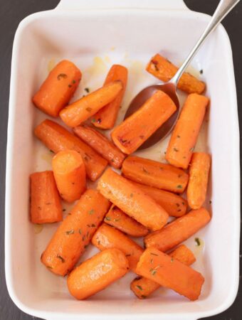 A casserole dish with roast honey glazed tarragon carrots and a serving spoon in.