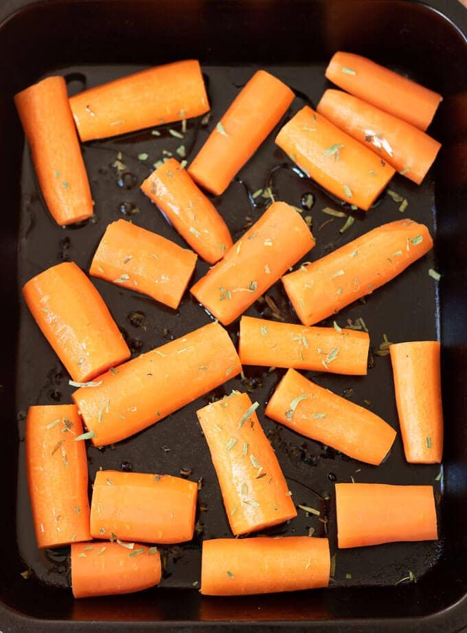 Birds eye view of a baking tray with carrots covered in tarragon ready to go into the oven.