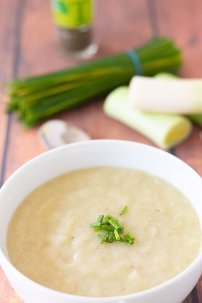 A delicious bowl of creamy vegan cauliflower leek soup with chives and leeks in the background served and ready to eat.
