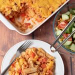 Top down view of sausage pasta bake served in a plate with the whole casserole in the background and a bowl of side salad to share.