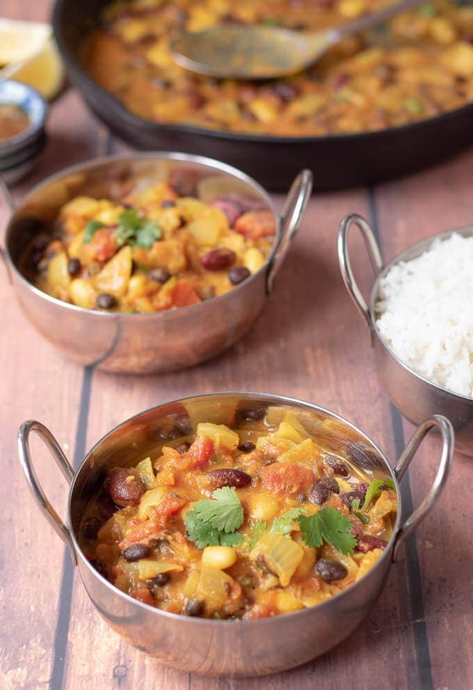 Vegan mixed bean curry in silver balti serving dishes ready to eat. 
