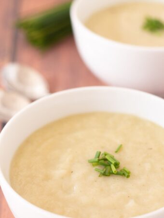 Two delicious bowls of creamy vegan cauliflower leek soup one in front of another garnished with chives served and ready to eat.