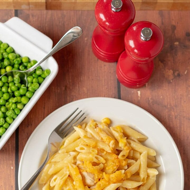 The best chicken and sweetcorn pasta bake served on a white plate with a side of peas beside and salt and pepper shaker behind.