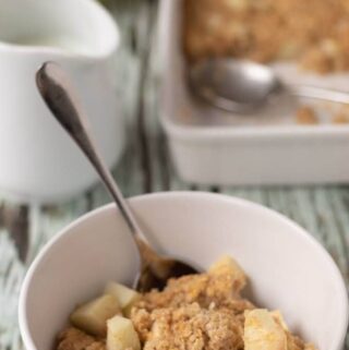 Bowl of cooked baked apple and cinnamon oats served with spoon in.