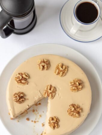 Birds eye view of coffee cheesecake with a slice taken out. Decorated with walnuts and a cafetiere and cup of coffee at the top.
