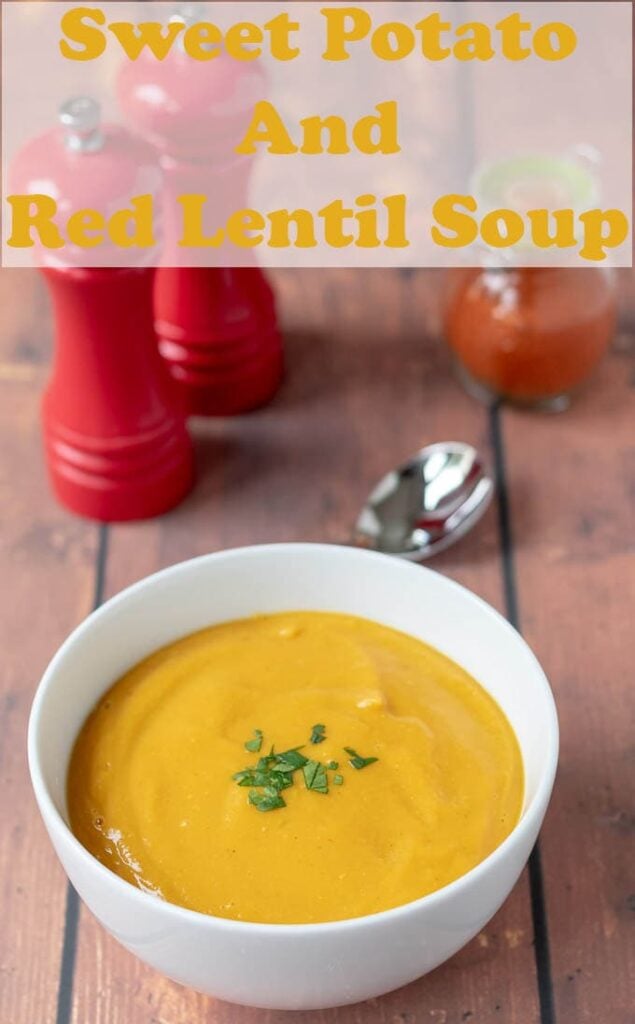 Bowl of sweet potato and red lentil soup with spoon, salt and pepper grinders and jar of red chilli powder in the background.