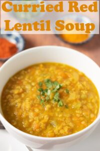 Close up of a bowl of curried red lentil soup garnished with chopped coriander. Pin title text overlay at top.