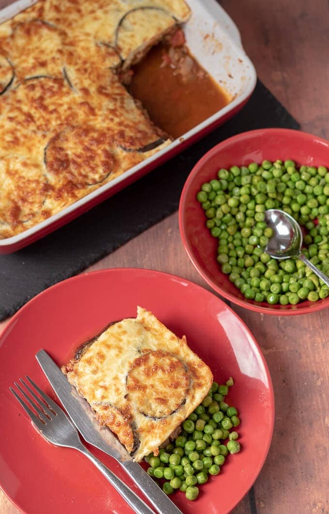 Birds eye view of a slice of healthier Moussaka on a plate with a serving of peas.