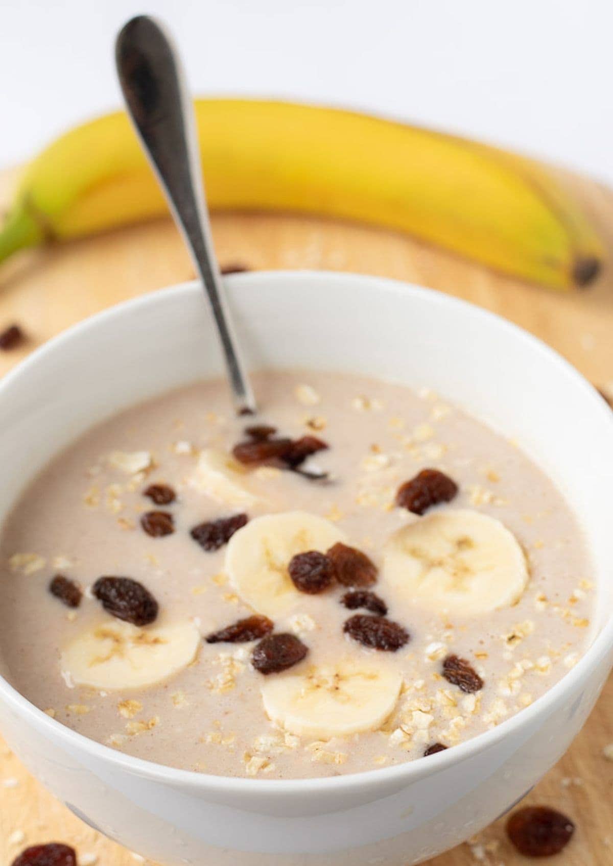 A bowl of delicious banana cinnamon overnight oats topped with slices of banana and a spoon in, ready to eat with a banana in the background as decoration.