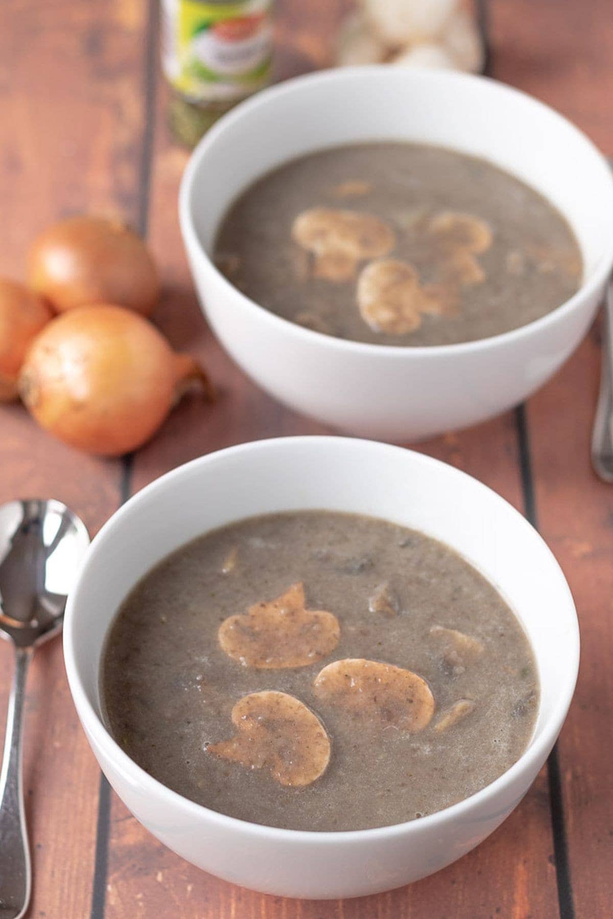 Two bowls of mushroom tarragon soup one in front of the other garnished with sliced mushrooms.
