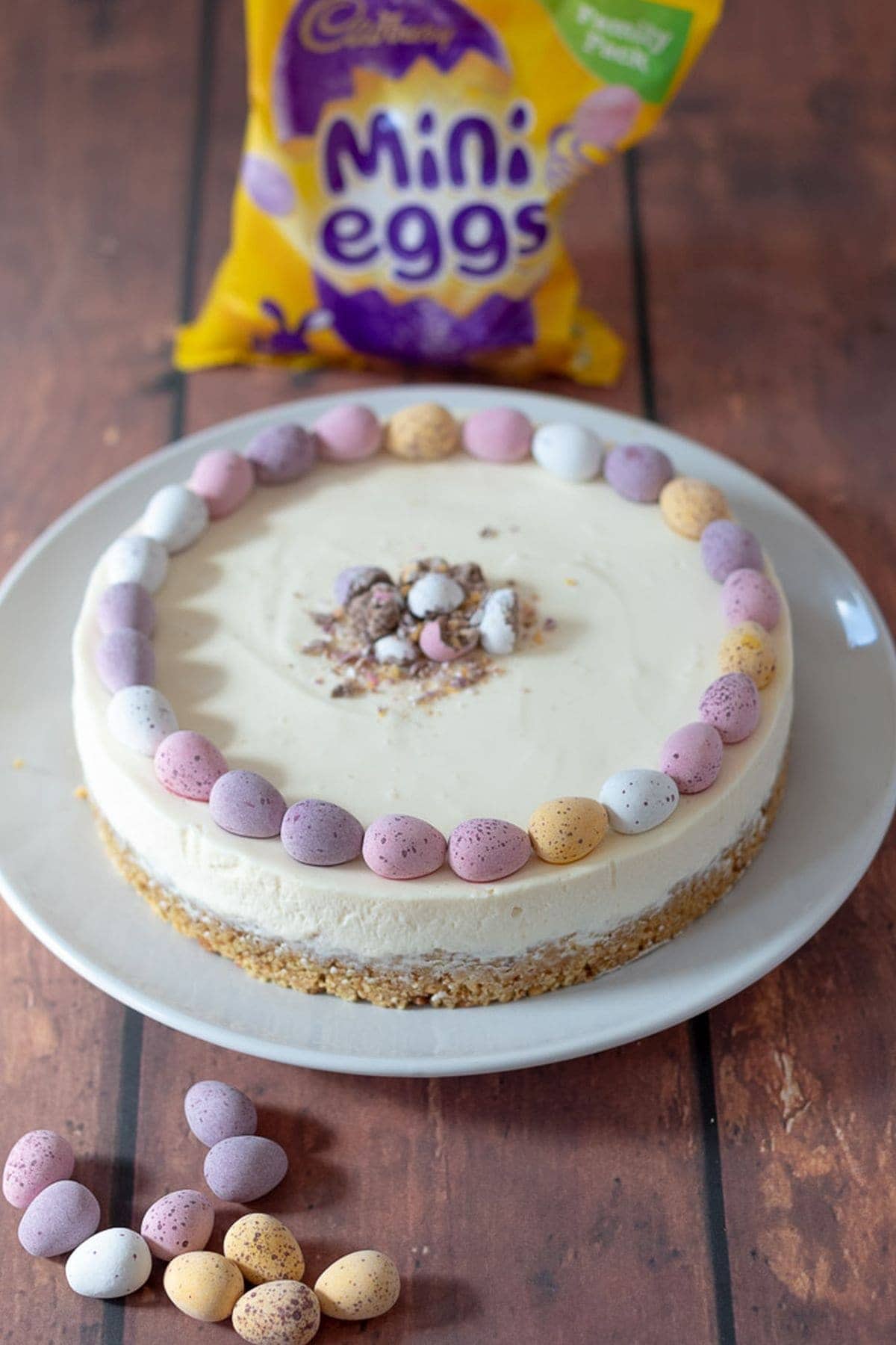 Freshly decorated easy no-bake mini egg Easter cheesecake ready to be sliced and served with a packed of mini eggs in the background.